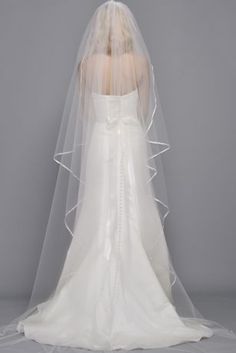 the back of a bride's wedding dress with a veil over her head and shoulder