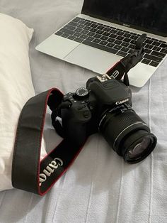 a laptop computer sitting on top of a white bed next to a camera and lens