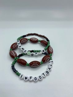 three beaded bracelets with the word football written in white and green letters on them