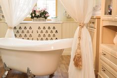 a white bath tub sitting in a bathroom next to a window with curtains on it