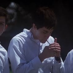 three young men standing next to each other with their hands together and looking at something