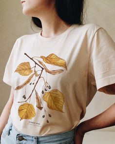 T-shirt featuring a botanical illustration of fall Linden tree (Tilia cordata). Fall in love with our autumn leaves shirt that you won't find anywhere else. Printed on a cream t-shirt, made from durable lightweight cotton. Unisex fit - boxy and long. How it's made: * All prints are original watercolor designs hand-painted by a botanical artist. * Ethically made 100% cotton t-shirts that are made to last. * T-shirts are printed and shipped by my printing partner in the US, Canada, or Europe. * By buying from this shop you are directly supporting a woman-owned small business, created out of love for plants to educate, inspire and keep us connected to the natural world. About the artist: This Shop is an extension of my botanical illustration studio, where I create hand-painted watercolor art Casual Cotton T-shirt With Watercolor Print, Nature-inspired Cotton Top With Plant Print, Nature-inspired Cotton Tops With Graphic Print, Botanical Relaxed Fit Tops For Fall, Nature-inspired Cotton Tops With Screen Print, Relaxed Fit T-shirt With Plants Print, White T-shirt With Fall Themed Plant Print, Nature-inspired Crew Neck Tops With Screen Print, White T-shirt With Plant Print For Fall