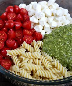 pasta, tomatoes and pesto sauce in a glass bowl on a wooden table top