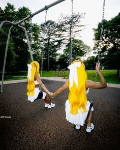 two women in yellow and white dresses sitting on swings at a park, one holding the other's hand