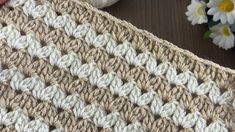 a crocheted blanket sitting on top of a wooden table next to white flowers