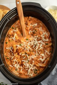 a crock pot filled with meat and cheese on top of a table next to bread