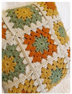 a crocheted blanket with orange, green and yellow flowers on it sitting on a white surface