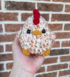 a hand holding a small crocheted chicken with a red hat on it's head