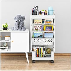 a white book shelf filled with books next to a small desk and toy elephant sitting on top of it