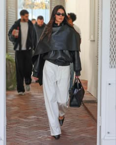 a woman in white pants and black jacket walking down the street with a handbag