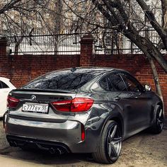 two cars parked next to each other in front of a brick wall and tree with no leaves