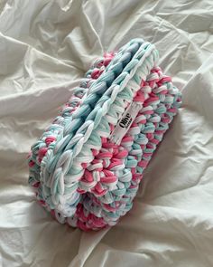 a stack of multicolored towels laying on top of a white sheet covered bed