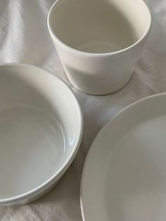 three white bowls sitting on top of a bed next to each other with one bowl in the middle