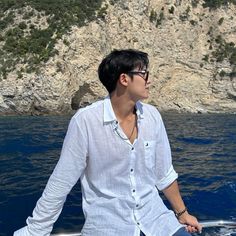 a man sitting on top of a boat in the ocean next to a rocky cliff