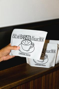 a person holding up two bags with coffee on them in front of a wooden table