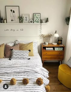 a white bed topped with lots of pillows next to a yellow chair and table filled with plants