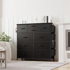 a black dresser in a white room with a plant on the floor and other furniture