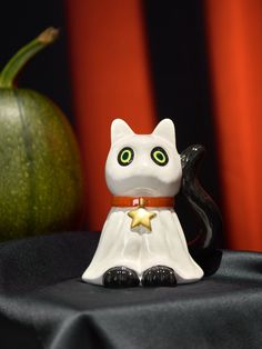 a white cat figurine sitting on top of a table next to a pumpkin