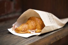 a croissant wrapped in wax paper on top of a wooden table