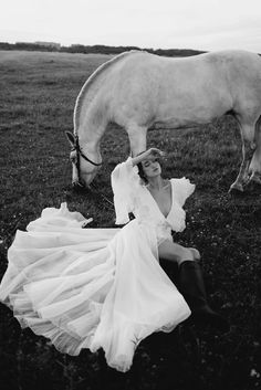 a woman sitting on the ground next to a white horse in a black and white photo