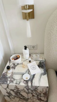 a marble topped table with bottles and soaps on it next to a white chair