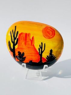 a painted rock sitting on top of a white surface next to a tree and mountain