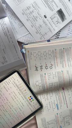 an open book sitting on top of a table next to papers and a tablet computer