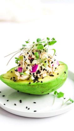 an avocado on a white plate topped with sprouts and other toppings