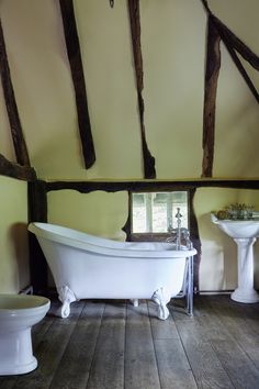 an old fashioned bathtub and pedestal sink in a bathroom with exposed wood beams on the ceiling