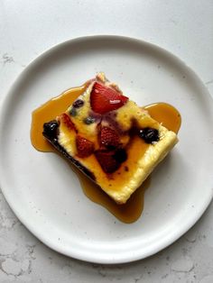 a piece of cake on a white plate covered in syrup and strawberries with sauce