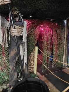 a fake skeleton holding a broom standing in front of a wall covered with plants and vines