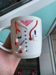 a hand holding a white coffee mug with red and blue stethoscopes on it