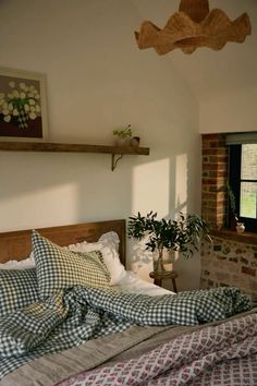 a bed with plaid sheets and pillows next to a potted plant in a window sill