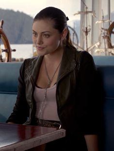 a woman sitting at a table in front of a wooden boat steering wheel on the water