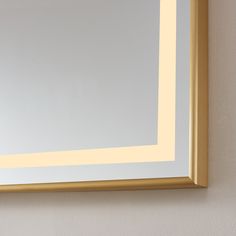 a bathroom mirror that is reflecting the light on it's side wall, with a gold frame