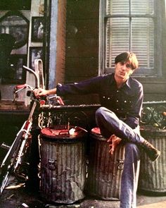 a man sitting on the back of a motorcycle next to trash cans and a bike