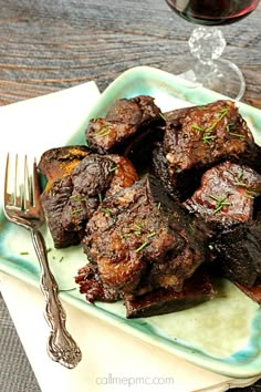 a plate with some meat on it next to a glass of wine and a fork