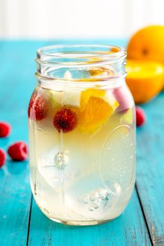 a glass jar filled with liquid and fruit on top of a blue table next to lemons