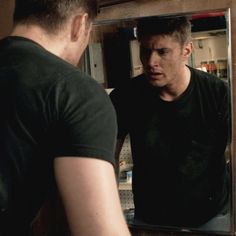 a man standing in front of a mirror looking at his own reflection on the wall