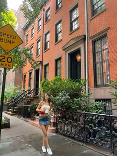 a woman is standing on the sidewalk in front of some brownstone apartment buildings with a speed bump sign