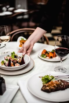 a person reaching for food on a plate at a table with wine glasses and plates