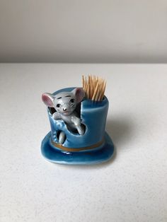 a small toy mouse in a blue cup on a white table with some brown sticks sticking out of it