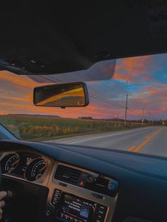 the driver is driving down the highway at sunset or dawn, with his hand on the steering wheel