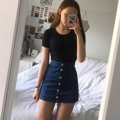 a woman taking a selfie in front of a mirror while wearing a black shirt and denim skirt