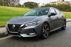 a gray car parked on the side of a road next to a green field and trees