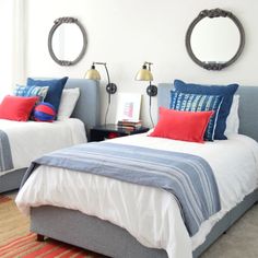 two beds in a bedroom with red and blue pillows on the headboards, one is made up