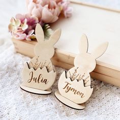 two wooden bunny ears with name tags on them sitting next to a bouquet of flowers