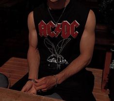 a man sitting on top of a wooden bench wearing a black shirt and silver bracelets