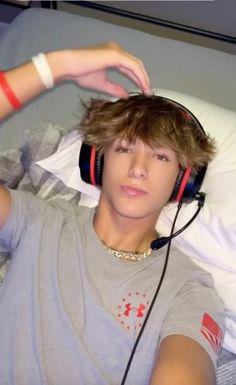 a young man wearing headphones while laying on top of a bed with his arm in the air