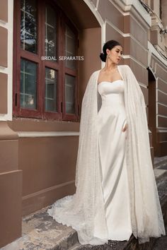 a woman in a white wedding gown and veil standing on the steps outside an old building